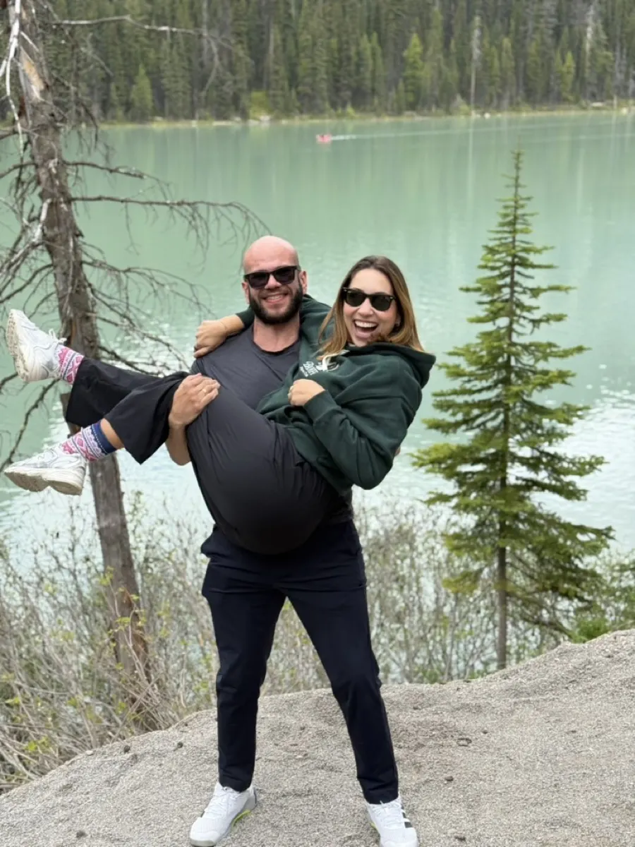 William carregando Fernanda no colo em frente a um lago
